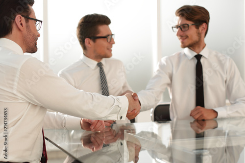 business partners shake hands while sitting at the table.