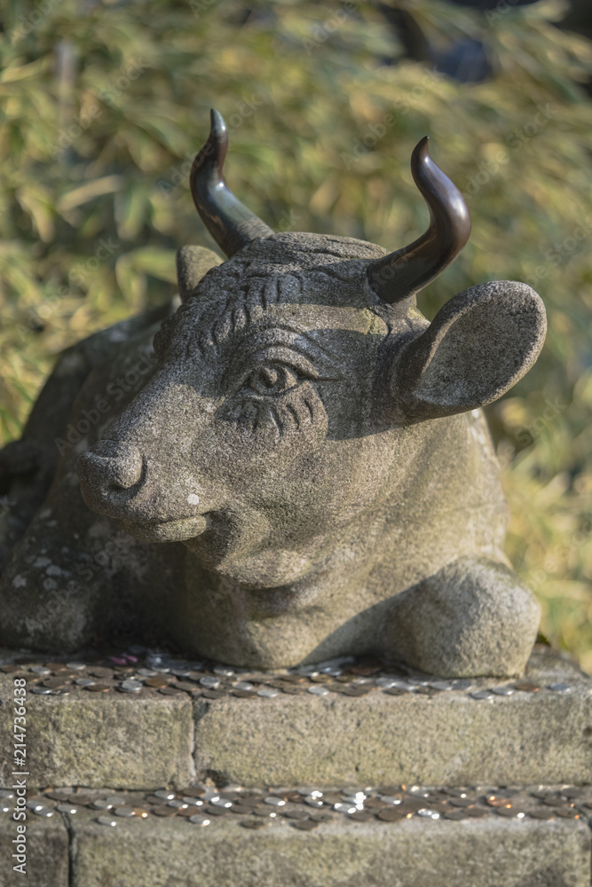 Obraz premium Buddhist stone statue of a bull lying with coins placed as an offering on his base in the Enryaku temple of Ryôgen monk in Hiei Mountain near Kyoto, Japan.