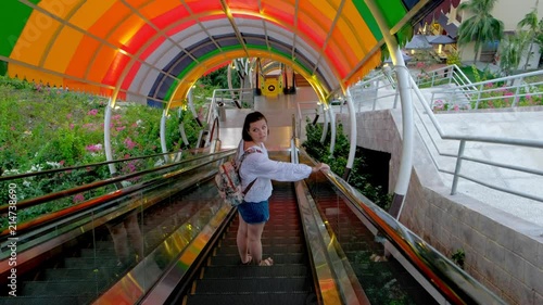 An aerial view of a pretty young woman going down by the colorful escalator in an entertainment park