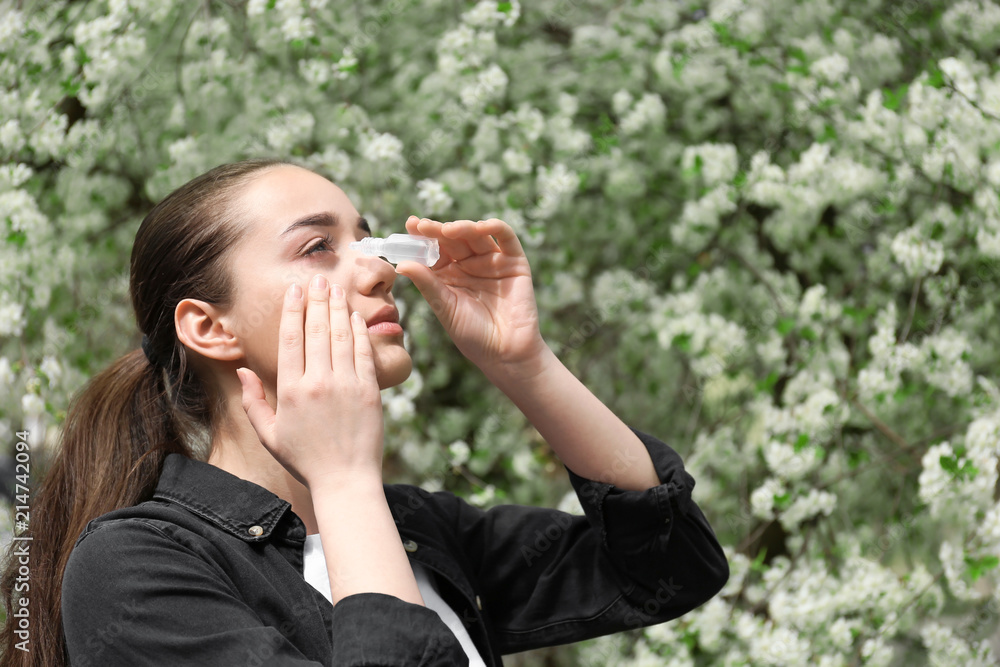 Young woman using eye drops near blooming tree. Allergy concept Young woman using eye drops near blooming tree. Allergy concept
