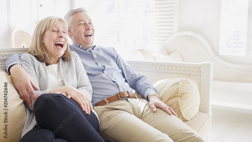 Portrait of smiling happy older couple laughing at something on their couch with space for text