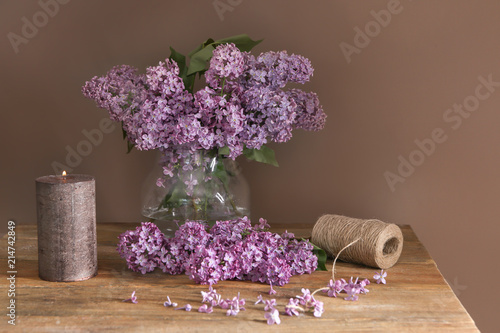 Vase with beautiful blossoming lilac and burning candle on table