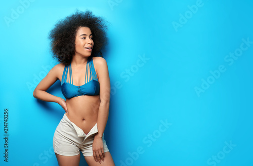 Beautiful African-American woman in bikini and shorts on color background