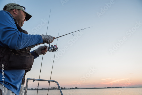 The fisherman with a spinning in his hands from the boat is catching fish at dawn. 