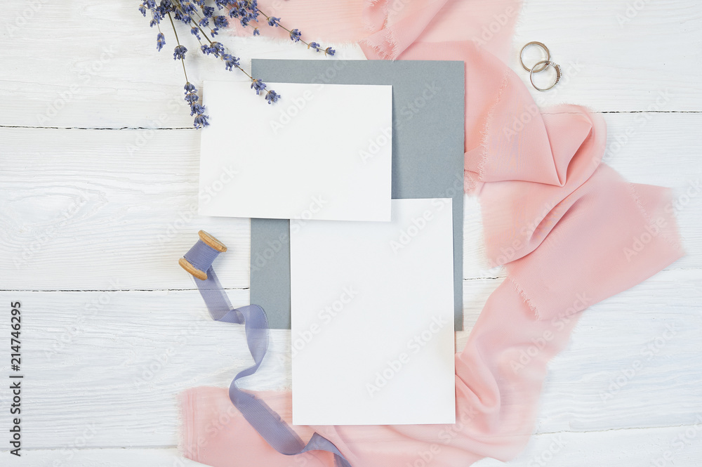 White blank card with two wedding rings on a background of pink fabric with lavender flowers and calligraphic pen on a white background. Mockup with envelope and blank card. Flat lay. Top view White blank card with two wedding rings on a background of pink fabric with lavender flowers and calligraphic pen on a white background. Mockup with envelope and blank card. Flat lay. Top view