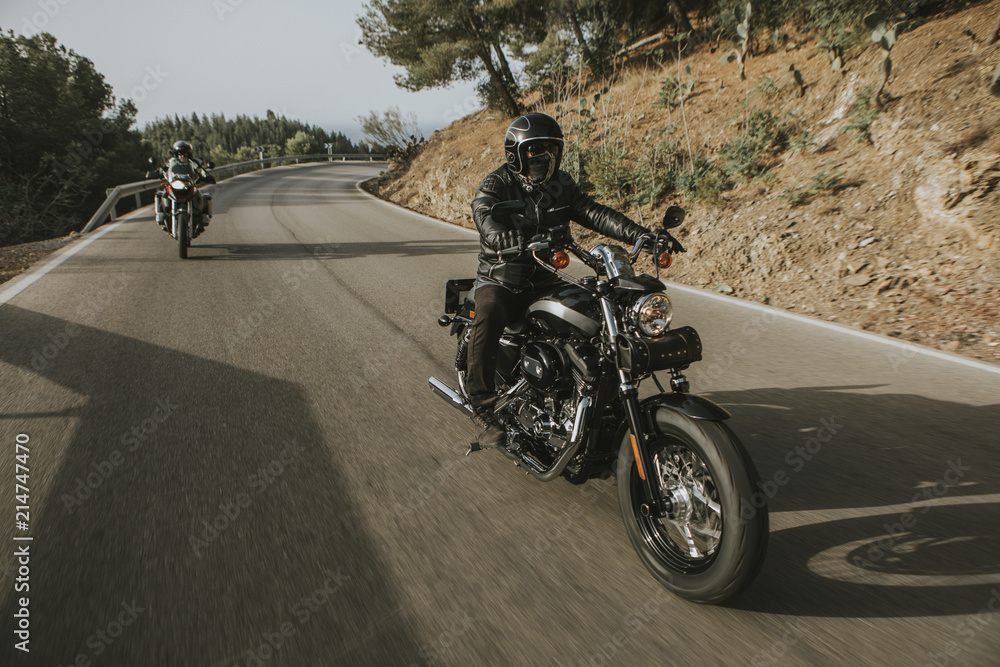 Man riding a black classic American motorcycle on the road in the mountains.