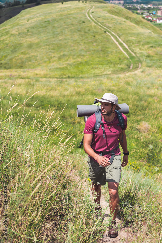 traveler in hat with backpack and tourist mat walking on path