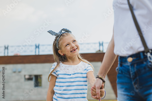 Smiling girl. Smiling preschool daughter without teeth looking at her mother while walking near river together