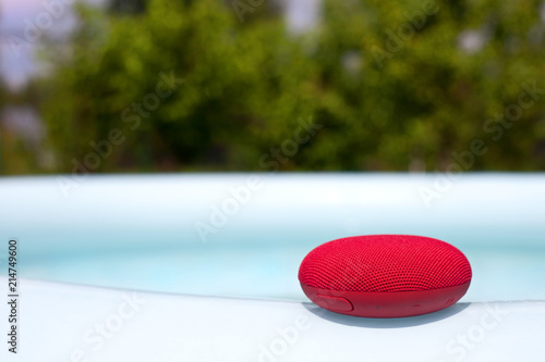 Red wireless speaker lying around the pool. photo