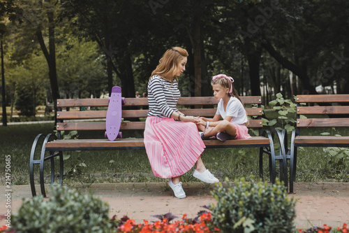 Fashionable mother. Fashionable mother wearing long pink skirt sitting on bench in the park near her daughter