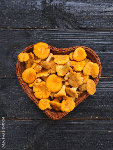 Orange chanterelle mushrooms lie in a wooden basket in the shape of a heart on a black background