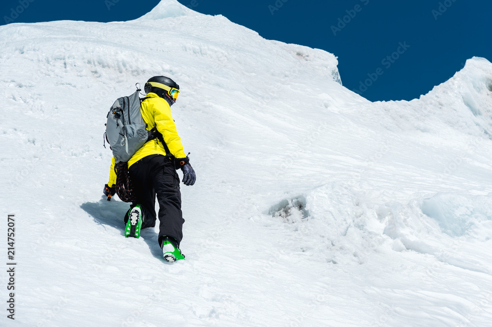 A skier in a helmet and mask with a backpack rises on a slope against the background of snow and a glacier. Backcountry Freeride