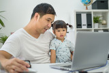 Man holding the kid  at the laptop, dad hugs a daughter, Asian family using the computer, Happy kid is smiling, Teaches his daughter to work with laptop. father and daughter looking at laptop at home
