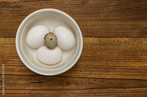 background. chicken and quail eggs in a white bowl on a wooden table