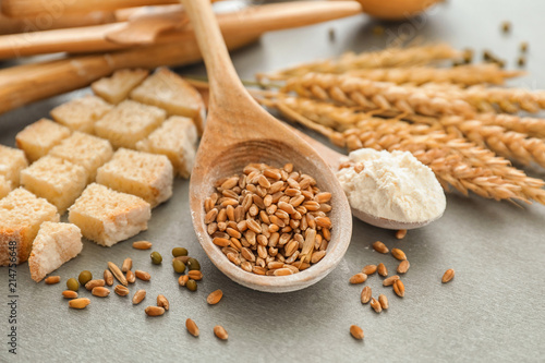 Spoons with wheat grains, flour and cut bread on table