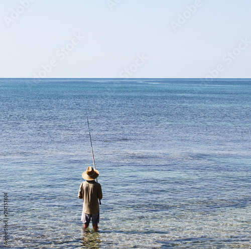 Fisherman with wide oriental style hat and fishing rod. seen from behind. Salento, Apulia, Italy
