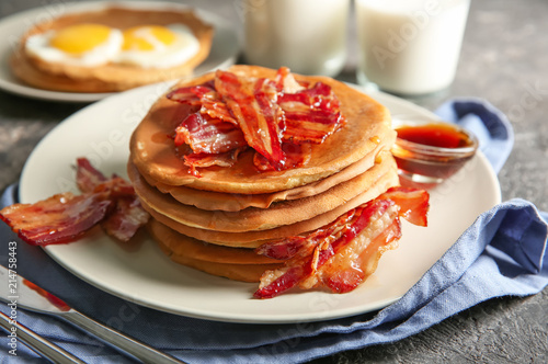 Plate with tasty pancakes and bacon on grey table
