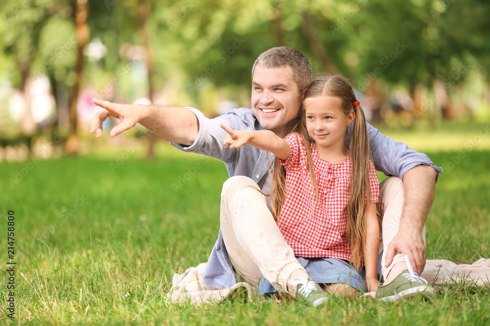 Happy father and daughter resting on plaid in green park