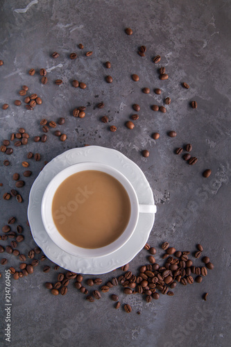  White cup of coffee with milk or tea with milk on dark grey beton background decorated with coffee beans. Copy space