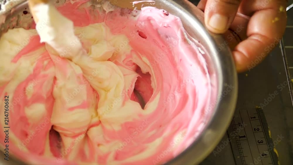 Hand stirring vanilla cream with pink in mixing bowl, slow motion Hand stirring vanilla cream with pink in mixing bowl, slow motion