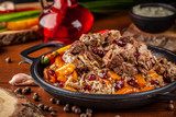 Uzbek traditional cuisine. Pilaf or plov with lamb, and red garnet, in an iron cast-iron frying pan kazan. Background image. Copy space, selective focus