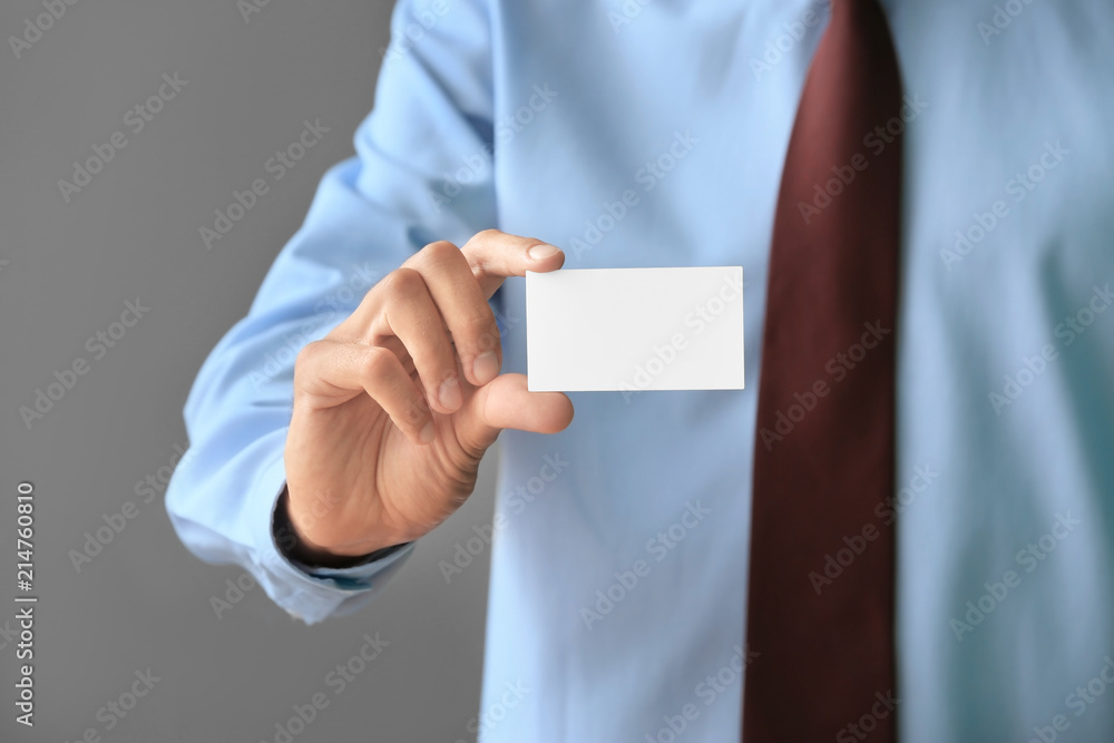 Man with business card on grey background, closeup