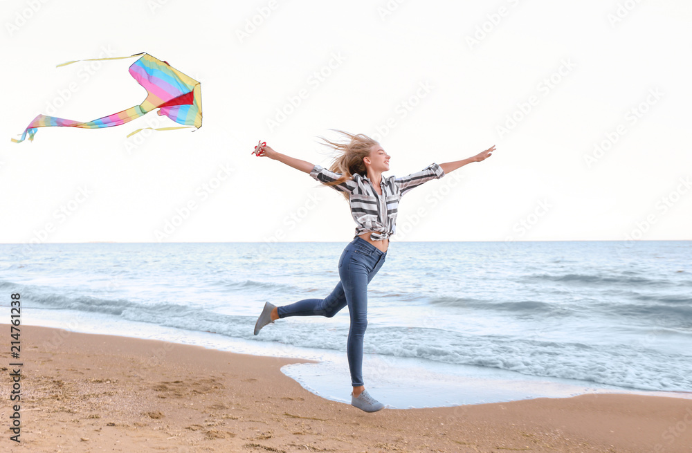 Obraz premium Beautiful young woman flying kite near sea