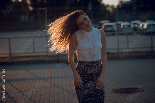 Young beautiful woman in stylish clothes whipping hair outdoors on sunset. Urban area background photo