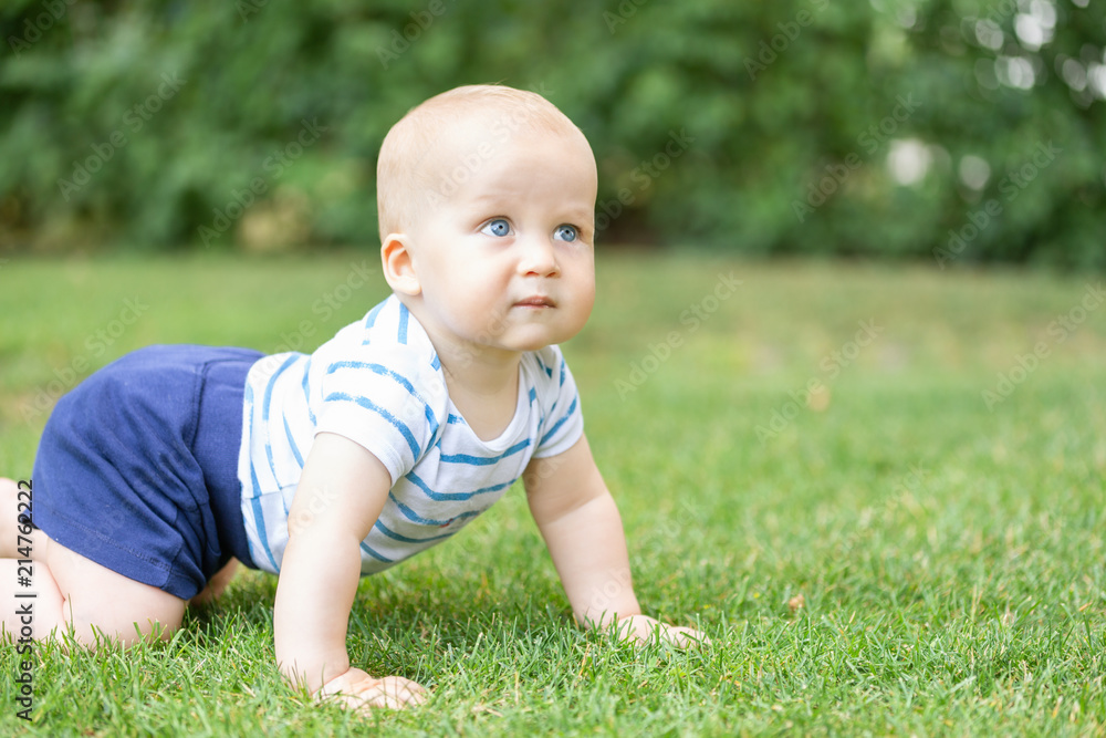 Portrait of cute blond pensive baby boy crawling on green grass lawn outdoors. Thoughtful kid thinking about something. Question or idea in children mind concept Portrait of cute blond pensive baby boy crawling on green grass lawn outdoors. Thoughtful kid thinking about something. Question or idea in children mind concept