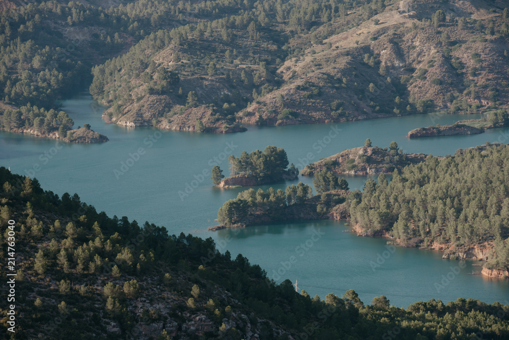 Emerald lake with little islands in the center of the valley covered with forest in the evening in Spain