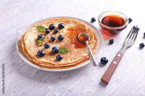 Plate with delicious thin pancakes, berries and syrup on wooden table