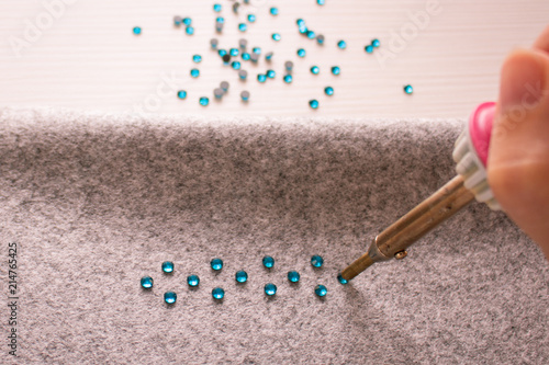 Handmade decoration. A process of soldering rhinestones on a gray cloth by soldering iron
