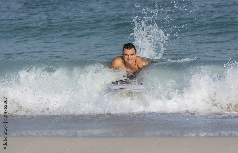 Muscular athletic white caucasian European male on Surfboard body surfing the splashing waves on a beach smiling happily Muscular athletic white caucasian European male on Surfboard body surfing the splashing waves on a beach smiling happily