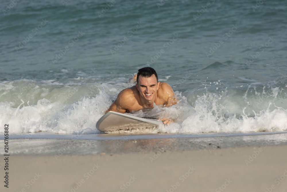 Muscular athletic white caucasian European male on Surfboard body surfing the splashing waves on a beach smiling happily