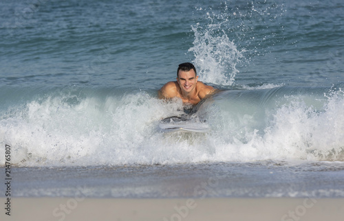 Muscular athletic white caucasian European male on Surfboard body surfing the splashing waves on a beach smiling happily © Paul