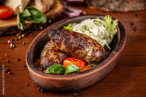 Uzbek traditional oriental cuisine. Lulya kebab from ground beef with pickled onion, salad, cherry tomatoes in a dish of red clay. Background image. Copy space, selective focus photo