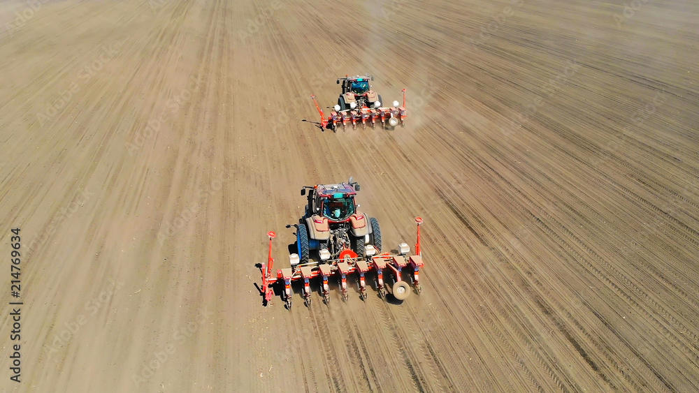 Fototapeta premium Aerial view of a farmers in two tractors seeding, sowing agricultural crops at field