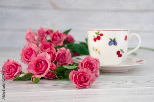 A cup of coffee on a saucer and small pink roses on a wooden table
