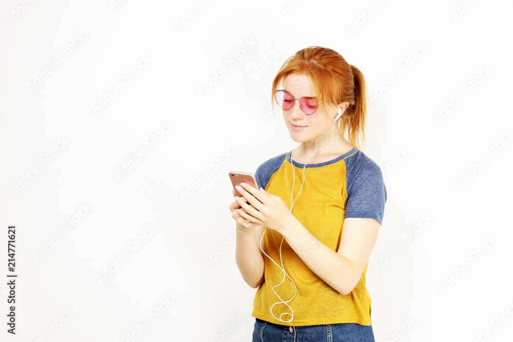 Young attractive natural redhead woman smiling, enjoying favorite song with hands free earphones. White background, copy space. Attractive red hair female in casual outfit listening to beloved tune. Young attractive natural redhead woman smiling, enjoying favorite song with hands free earphones. White background, copy space. Attractive red hair female in casual outfit listening to beloved tune.