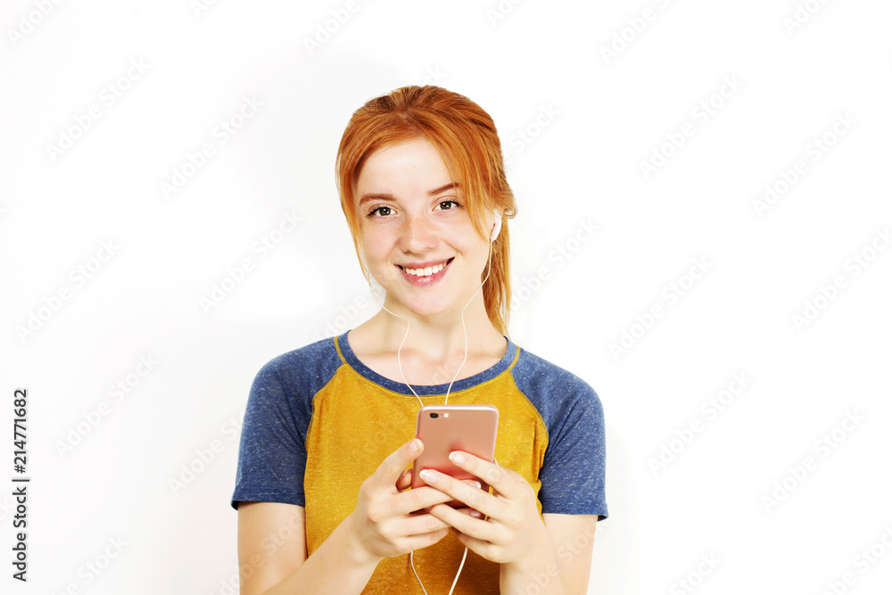 Young attractive natural redhead woman smiling, enjoying favorite song with hands free earphones. White background, copy space. Attractive red hair female in casual outfit listening to beloved tune. Young attractive natural redhead woman smiling, enjoying favorite song with hands free earphones. White background, copy space. Attractive red hair female in casual outfit listening to beloved tune.