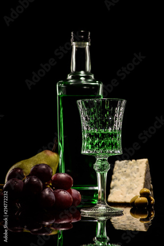 close-up shot of absinthe with ripe fruits and cheese on mirror surface on black