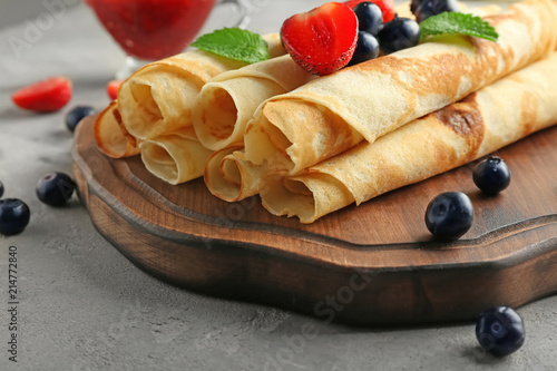 Board with tasty pancakes and berries on light table, closeup