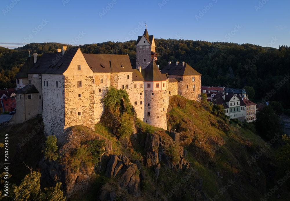 Aerial view on Loket Castle, Burg Elbogen, 12th-century Gothic style castle on a big rock, massive fortification illuminated by setting sun. Tourist place close to Karlovy vary, Czech republic.