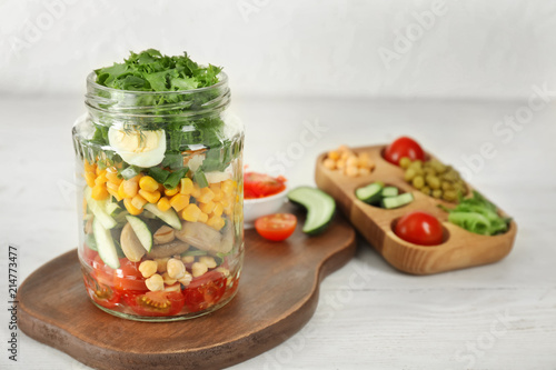 Delicious vegetable salad in mason jar on wooden board