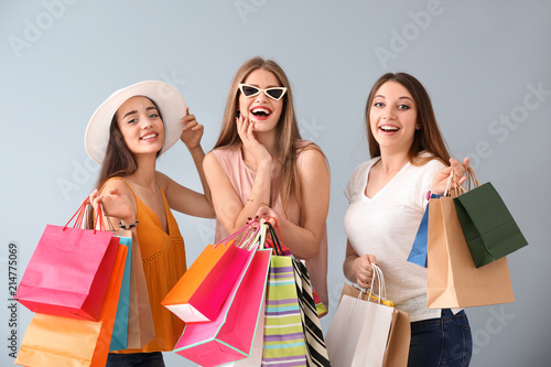 Beautiful young women with shopping bags on light background