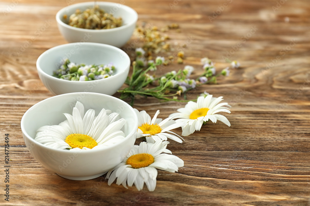 Beautiful chamomile flowers with bowls on wooden background