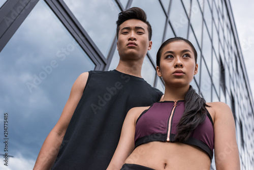 low angle view of serious asian sportsman and sportswoman standing at urban street