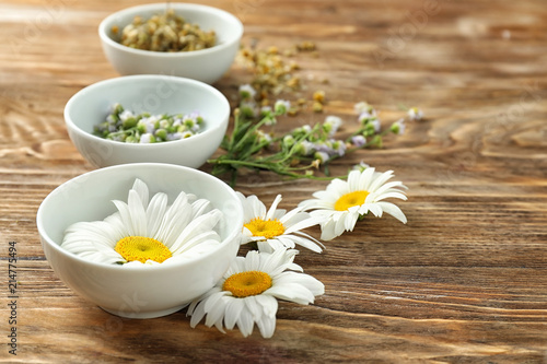 Beautiful chamomile flowers with bowls on wooden background