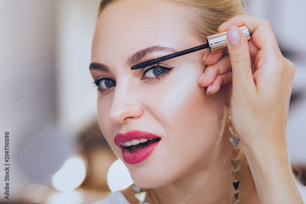 Coloring eyelashes. Blonde-haired appealing woman with dental brackets coloring her eyelashes Coloring eyelashes. Blonde-haired appealing woman with dental brackets coloring her eyelashes