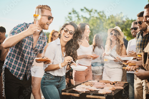 Foto Group of people standing around grill, chatting, drinking and eating